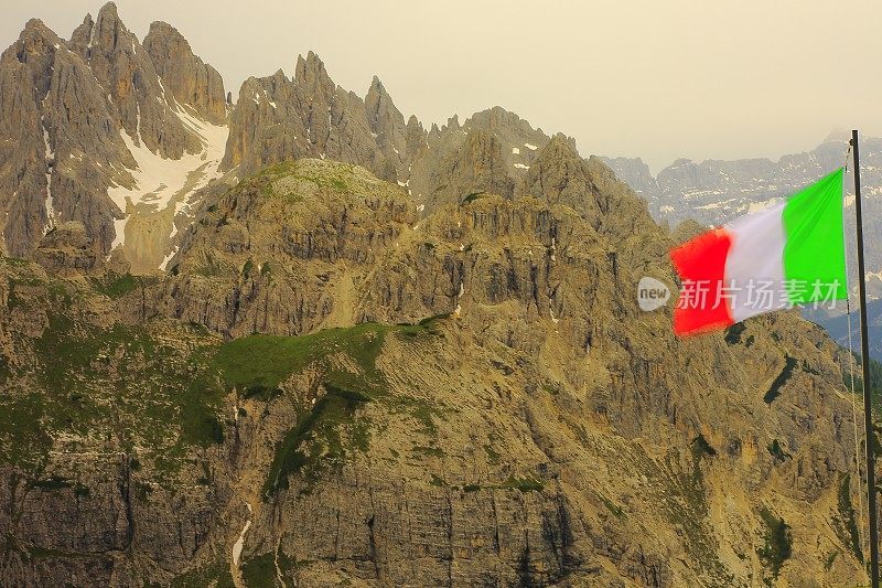 爱国主义:意大利国旗盘旋在田诗式的拉瓦雷多峰和Auronzo di cadore山脉和普斯特山谷，在穆迪日出日出时戏剧性的天空，戏剧性的全景和雄伟的Dolomites，意大利泰洛阿尔卑斯山